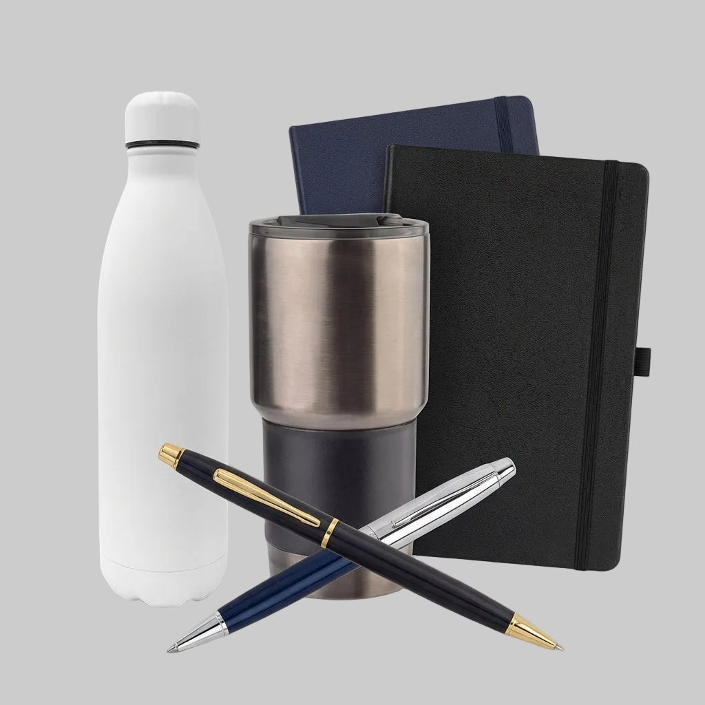 A promotional product bundle on a light gray background featuring a matte white insulated bottle, a brushed stainless steel travel tumbler, a black elastic-band notebook, and two pens crossed in front (one black with gold trim, one silver with gold trim).
