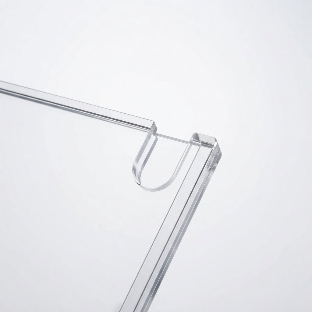 Close-up of a transparent acrylic or glass frame corner with a U-shaped hook or loop detail, shown on a clean white background.