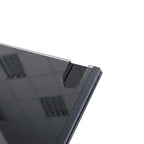 Close-up of a dark gray or black tablet or monitor corner with a glossy screen and a small transparent protective film along the edge, set against a light gray background.
