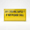 A bright yellow rectangular warning sign with black text that reads, 'AM I DRIVING SAFELY? IF NOT-PLEASE CALL:' inside a thin black border.