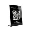 A black acrylic tabletop sign with a QR code, white text reading 'Please join our Whatsapp community for promotion updates' and fields for Name and phone number, shown on a light gray background.