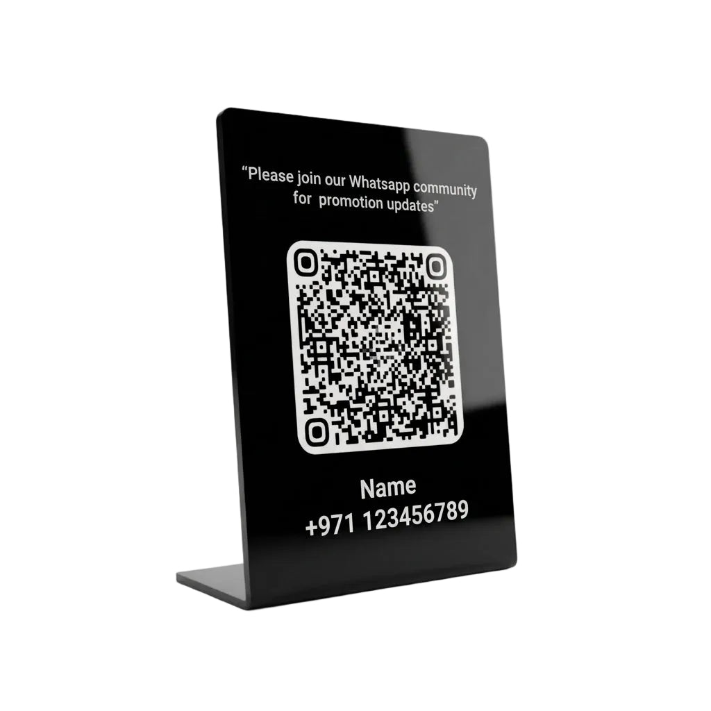 A black acrylic tabletop sign with a QR code, white text reading 'Please join our Whatsapp community for promotion updates' and fields for Name and phone number, shown on a light gray background.
