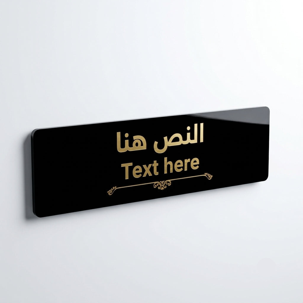 A glossy black rectangular wall sign with rounded corners, featuring gold Arabic and English text that reads 'النص هنا' and 'Text here' with a small decorative flourish below, shown against a light gray wall.