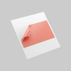 A square white card or sheet with a large coral-pink rectangular area partially peeled off, shown floating against a light gray studio background.