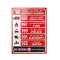 A rectangular emergency numbers sign in Arabic and English, with red, white, and black sections showing ambulance, fire, police, electricity, water, and no smoking emergency numbers on a white background.