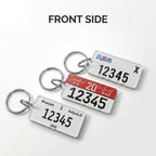 Three rectangular license plate keychains shown from the front on a light gray background, each attached to a silver metal key ring. The top keychain is white with blue and pink 'Dubai' text and black numbers; the middle keychain has a red header with white text and black numbers; the bottom keychain is white with black text.
