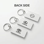 Three white rectangular car keychains with silver metal key rings, shown from the back side. The keychains feature the black logos of Nissan, Lexus, and Toyota, arranged diagonally on a light gray background with the text 'BACK SIDE' at the top.