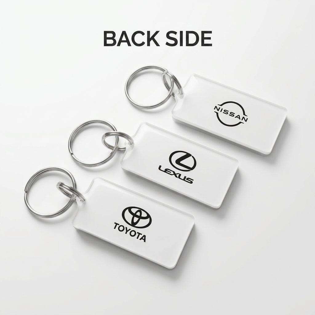 Three white rectangular car keychains with silver metal key rings, shown from the back side. The keychains feature the black logos of Nissan, Lexus, and Toyota, arranged diagonally on a light gray background with the text 'BACK SIDE' at the top.