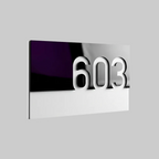 A modern rectangular house number plaque displaying '603' in large white 3D numerals, mounted on a reflective silver panel with a dark purple and black reflective section on the left, shown against a neutral gray background.